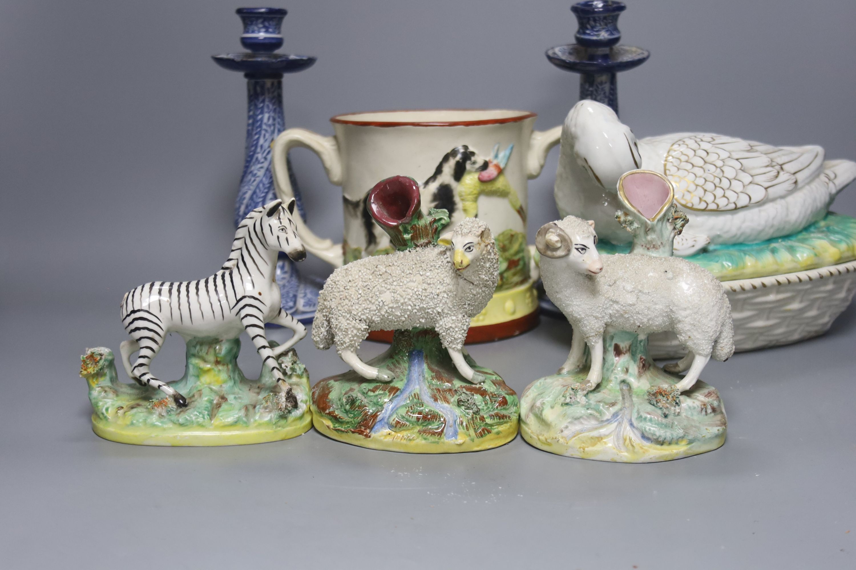 A Staffordshire pottery ‘duck’ tureen and cover, 23cm, a pair of faience candlesticks, Staffordshire figures of dogs, sheep and a zebra and a two handled loving mug